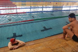 Rodrigo está dentro da piscina, apoiado na borda, conversando com Jean, que está sentado na beira da piscina