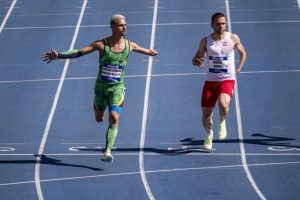 Na raia 5 da pista de atletismo, José Alexandre da Costa abre os braços ao cruzar a linha de chegada. Pouco atrás, na raia ao lado, corre o atleta Michal Derus